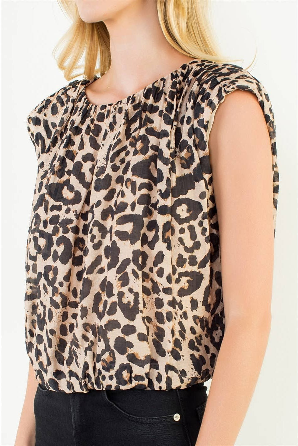 A woman wearing a sleeveless leopard-print top with a gathered, ruffled neckline and black pants, shown against a plain light background.