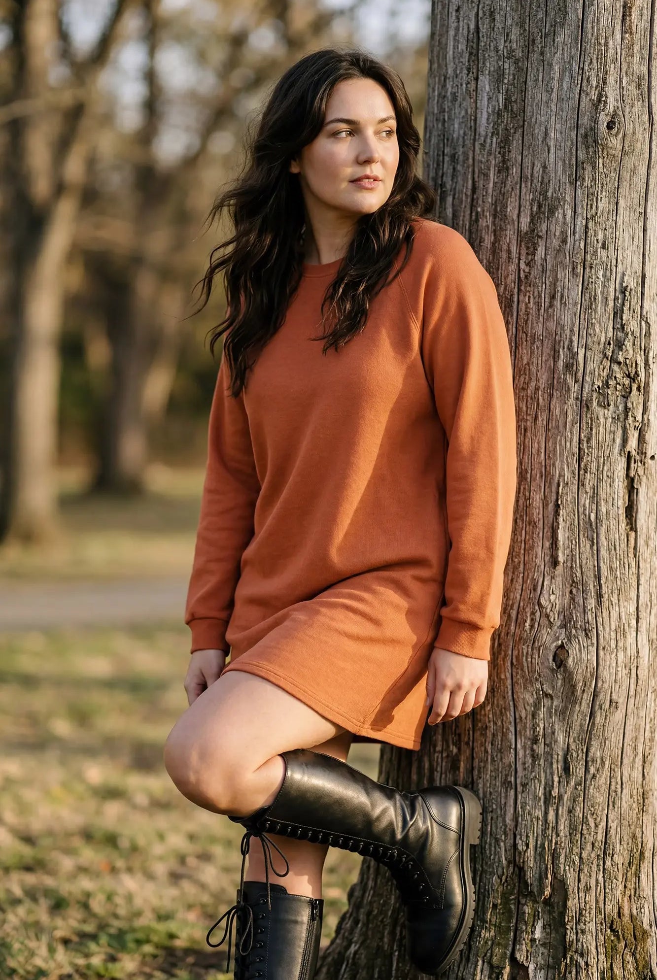 Model wearing orange dress and high boots against a tree