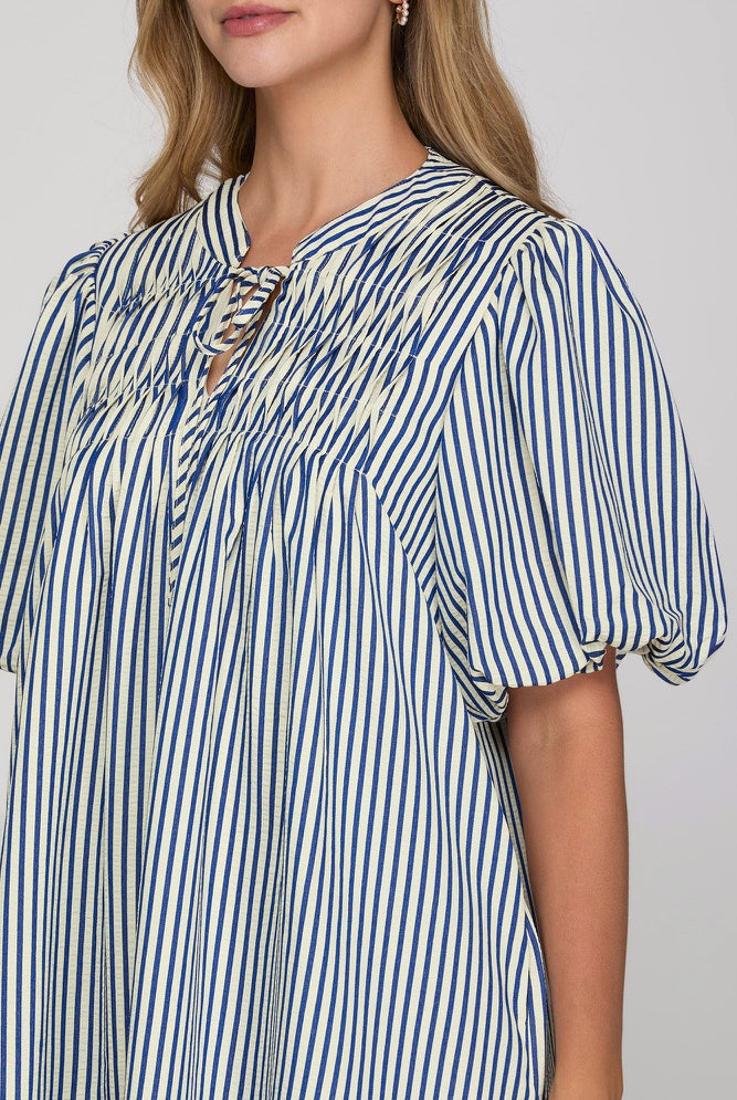A close-up of a woman wearing a blue and white vertically striped blouse with puff sleeves and a smocked neckline.