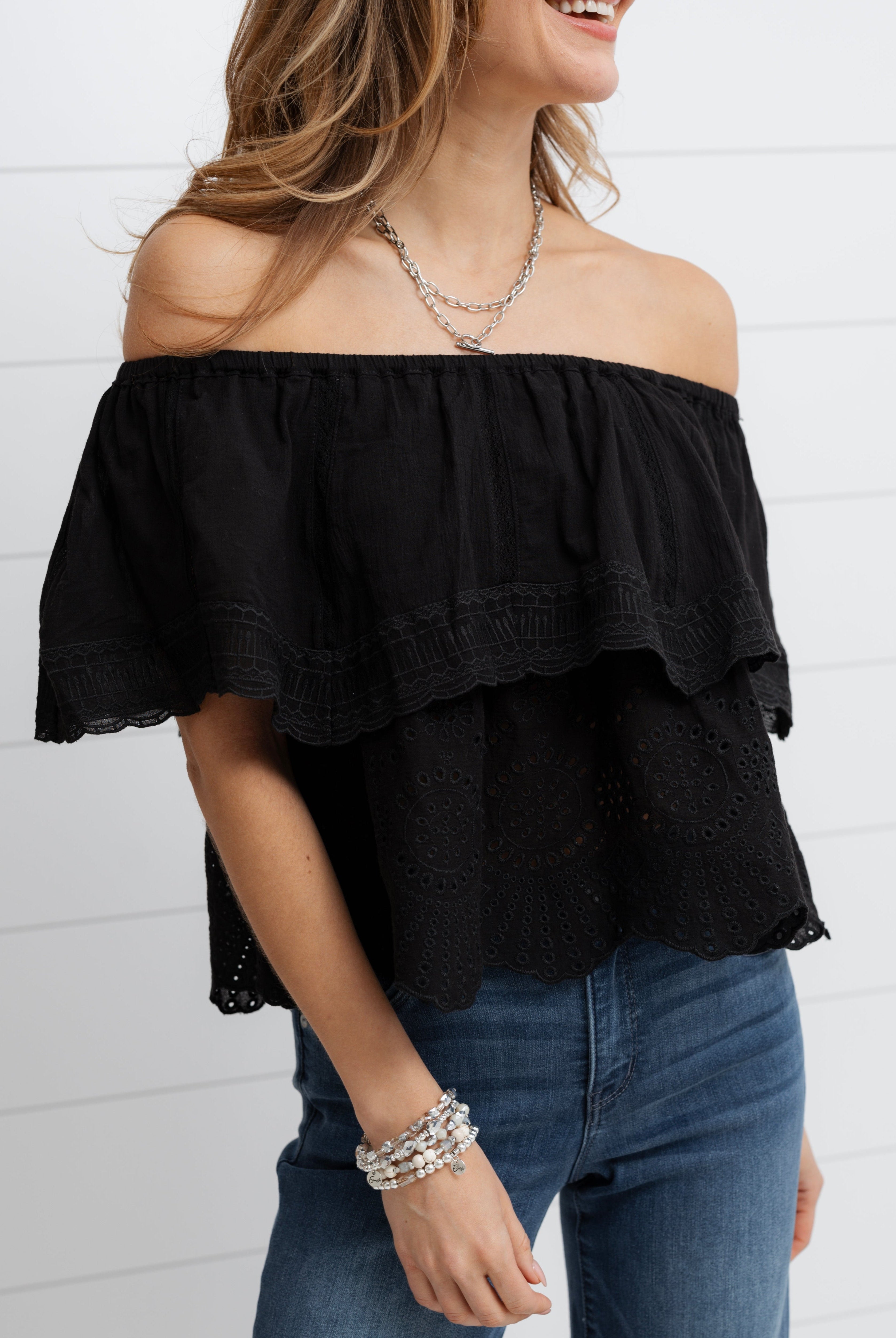 Woman wearing a black off-shoulder top and blue jeans against a white background