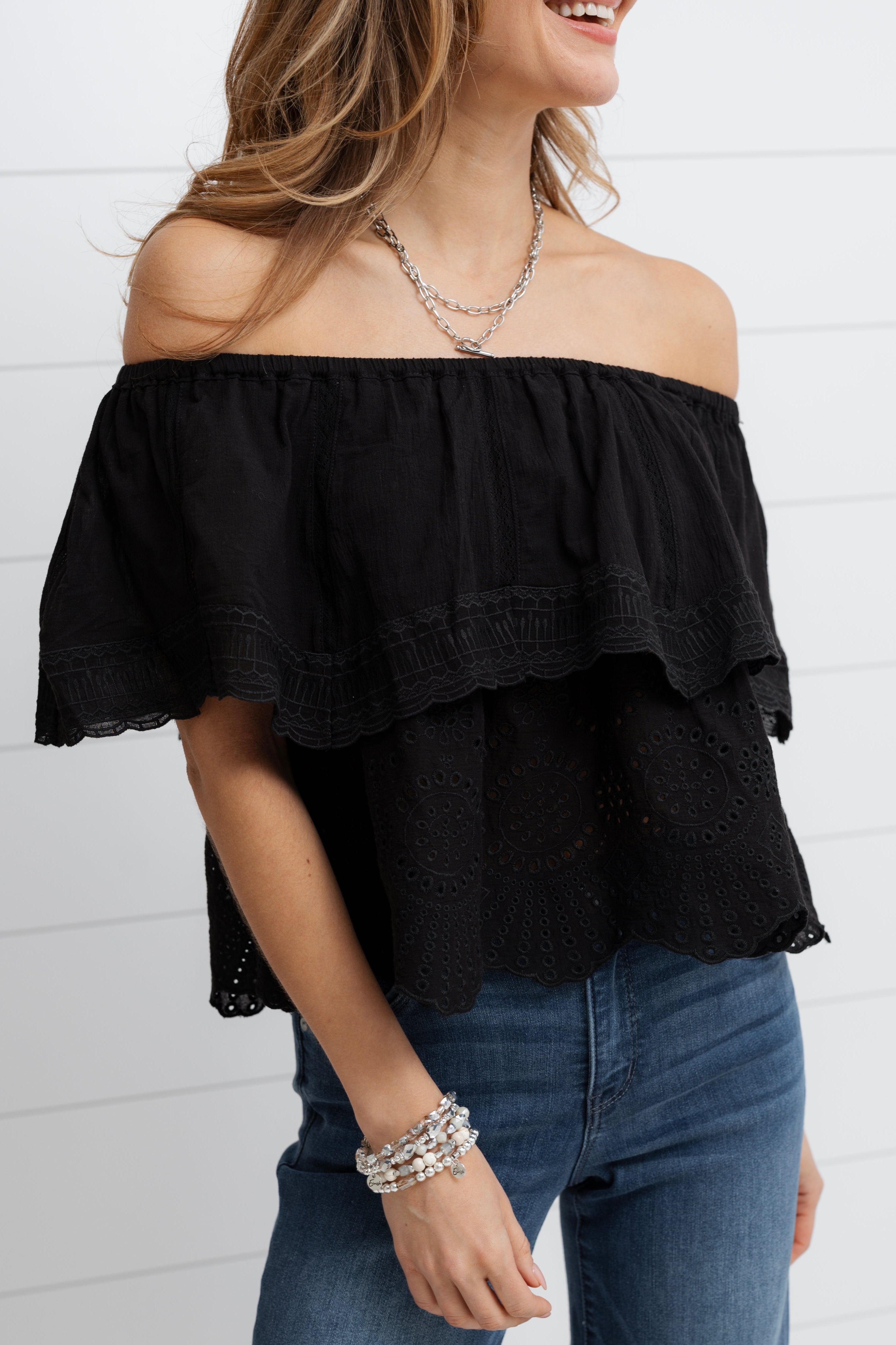Woman wearing a black off-shoulder top and blue jeans against a white background