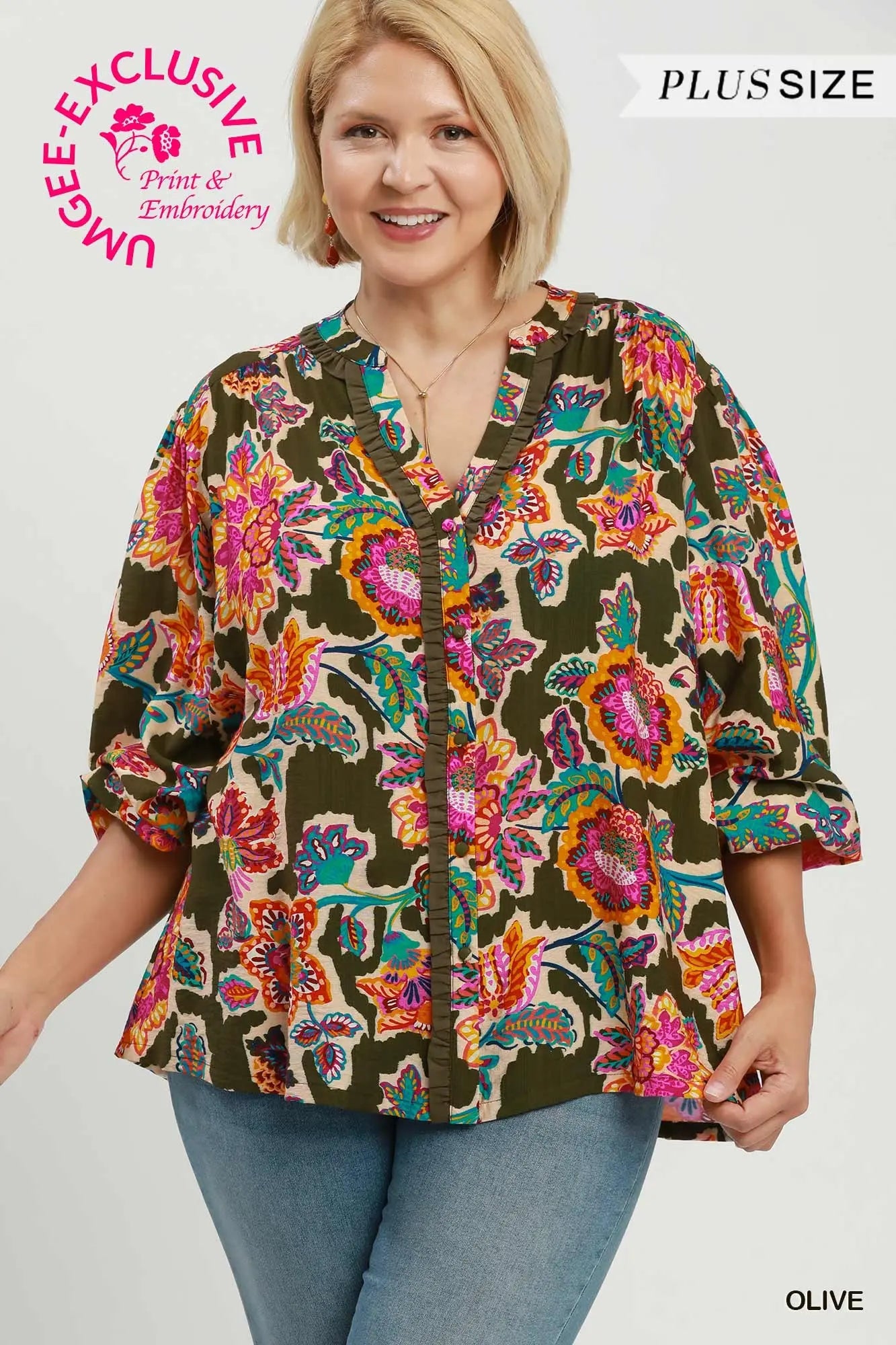 A woman wearing a short-sleeve button-front blouse with a colorful floral and paisley print over an olive base, paired with blue jeans. The image includes text overlays reading 'PLUS SIZE', 'OLIVE', and a circular 'UNIQUELY EXCLUSIVE Print & Embroidery' badge.