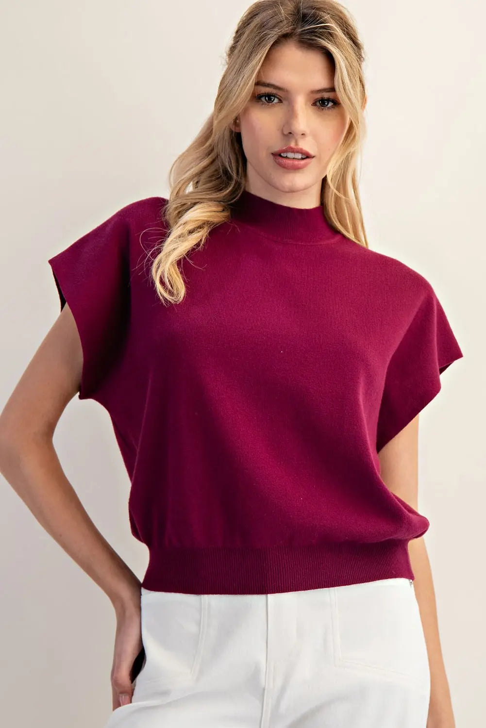 Model wearing plum mock neck tank with white pants