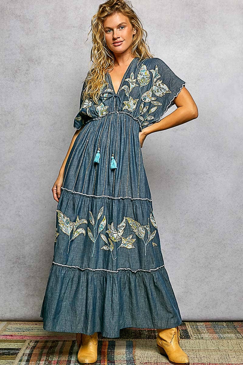 Woman wearing a blue embroidered dress with yellow boots against a gray background
