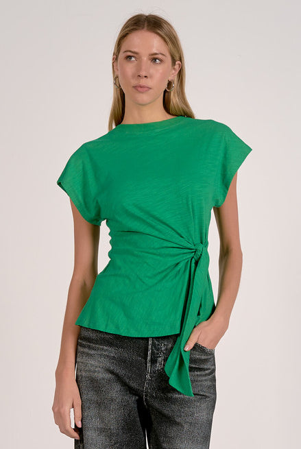 Woman wearing a green top with a tie detail on a plain background