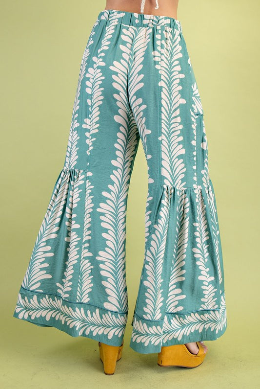 Mint wide-leg pants with white leaf pattern worn by a person on a green background