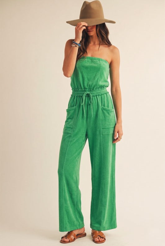 Woman wearing a green strapless jumpsuit and beige hat on a plain background