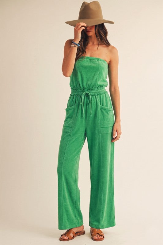Woman wearing a green strapless jumpsuit and beige hat on a plain background