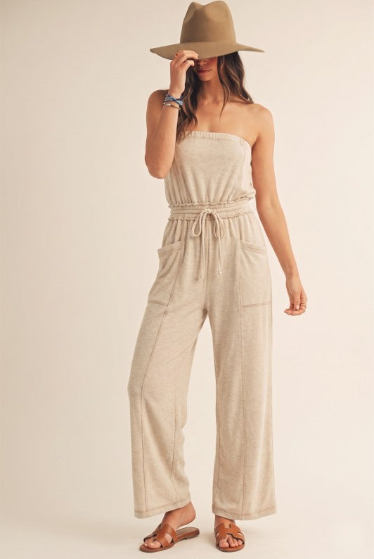 Woman wearing a beige strapless jumpsuit and hat on a plain background