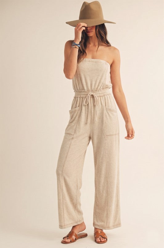 Woman wearing a beige strapless jumpsuit and hat on a plain background