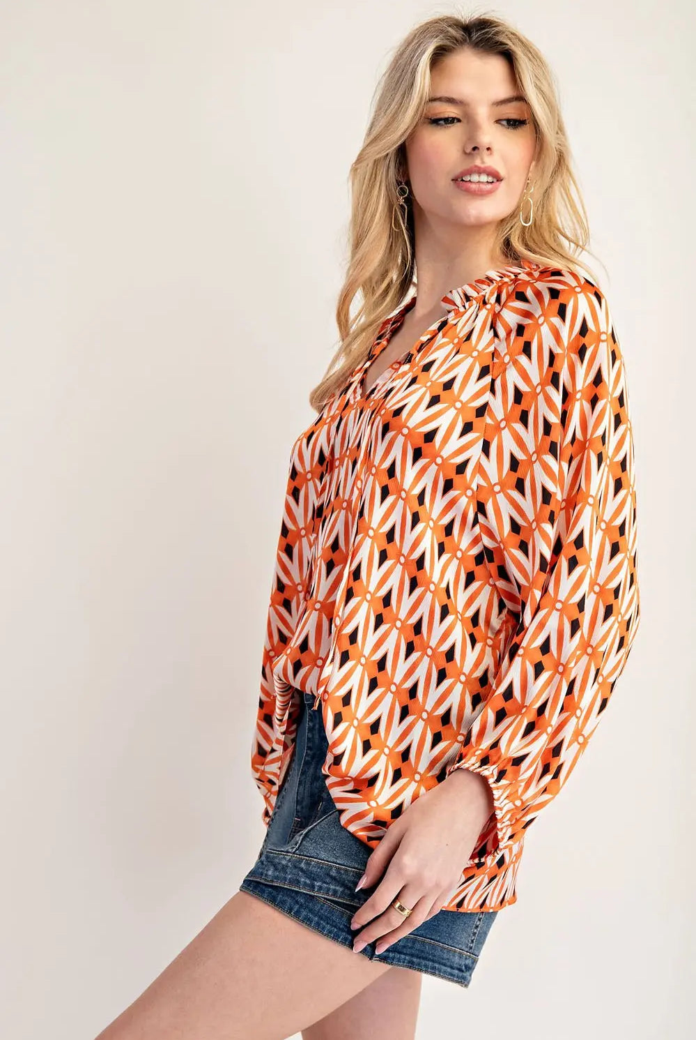 Side view of model wearing orange blouse with jean shorts