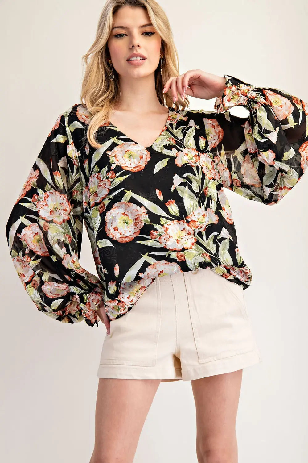 Model wearing black floral top with cream shorts