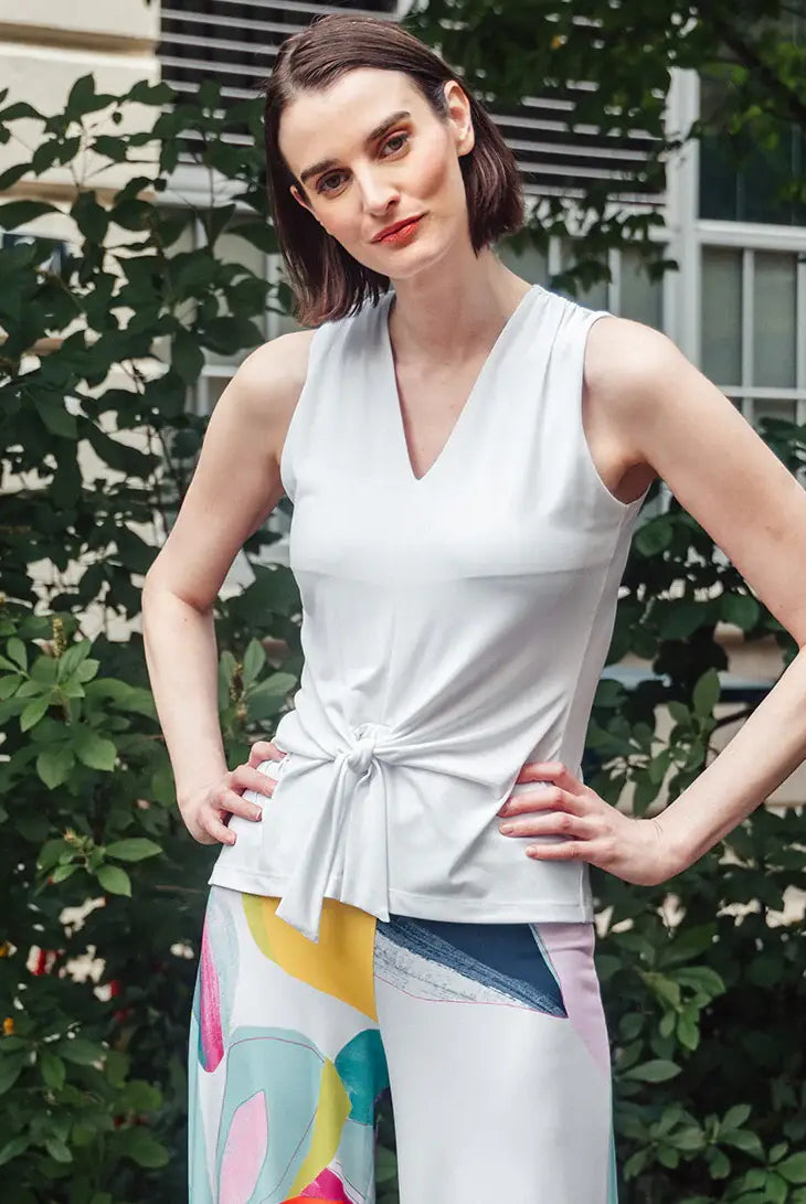 Model wearing white tank top with colorful pants against a bush