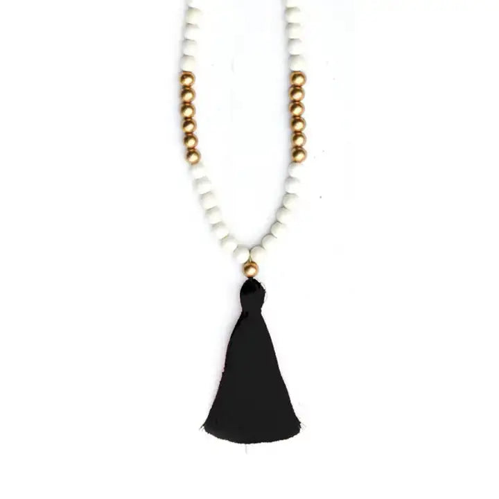 White and gold bead necklace with black tassel on a white background