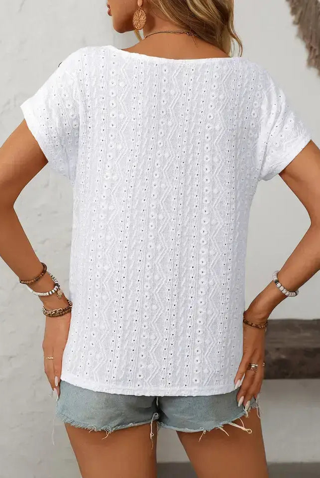 Person wearing a white short-sleeve top with a textured pattern and denim shorts against a neutral background.