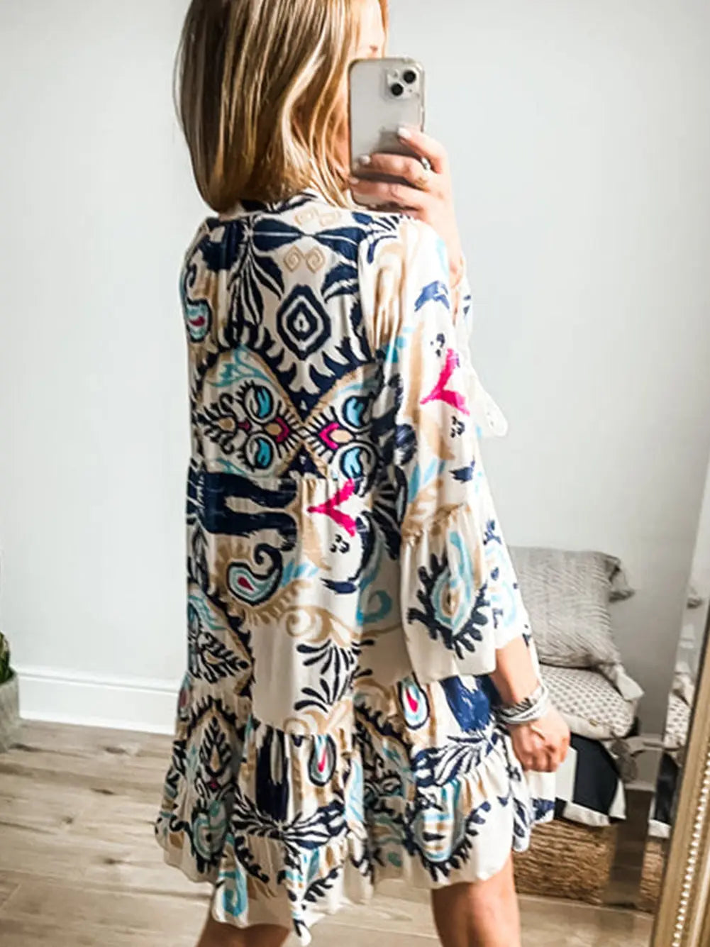 Woman wearing a colorful patterned dress taking a mirror selfie.
