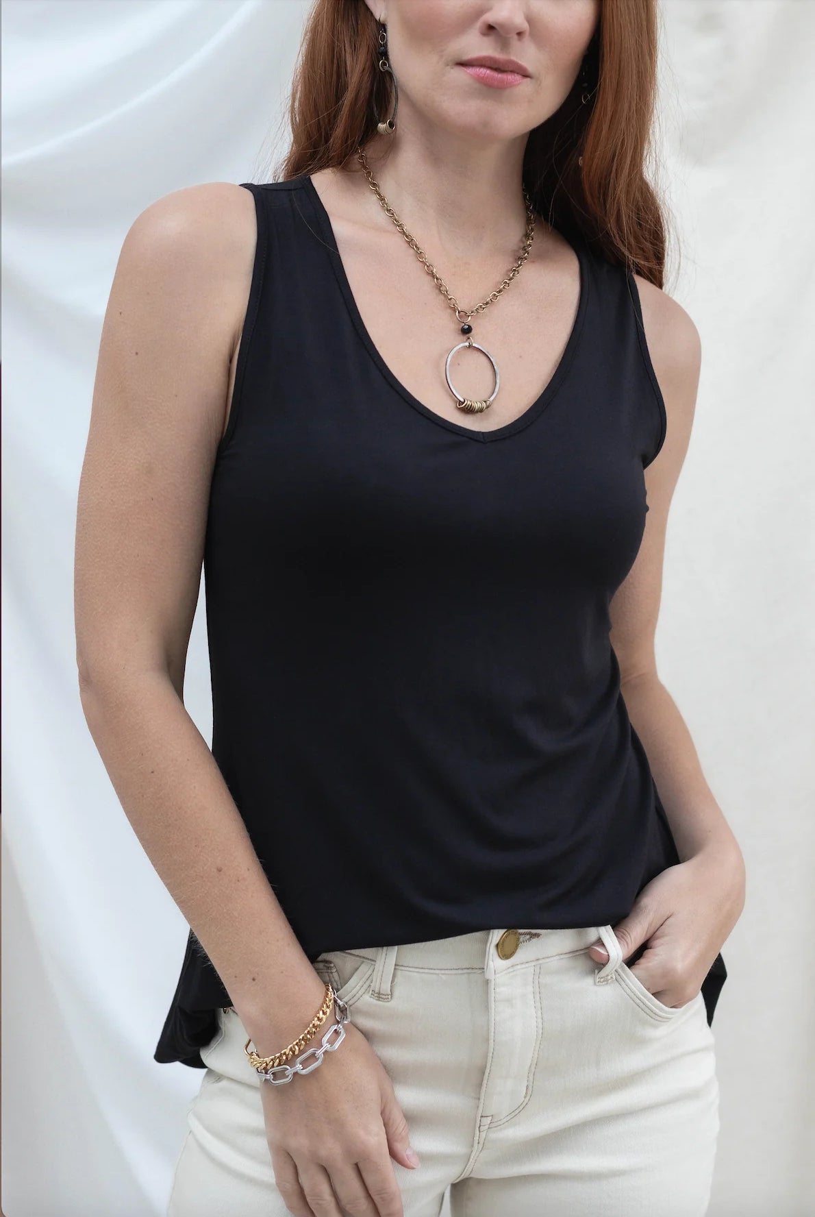 Woman wearing a black tank top and white pants against a plain background