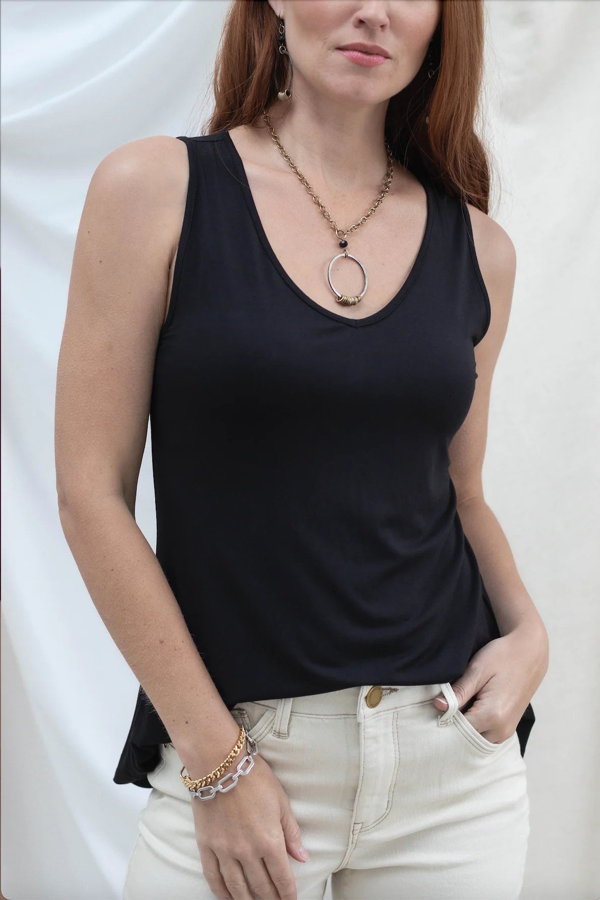 Woman wearing a black tank top and white pants against a plain background