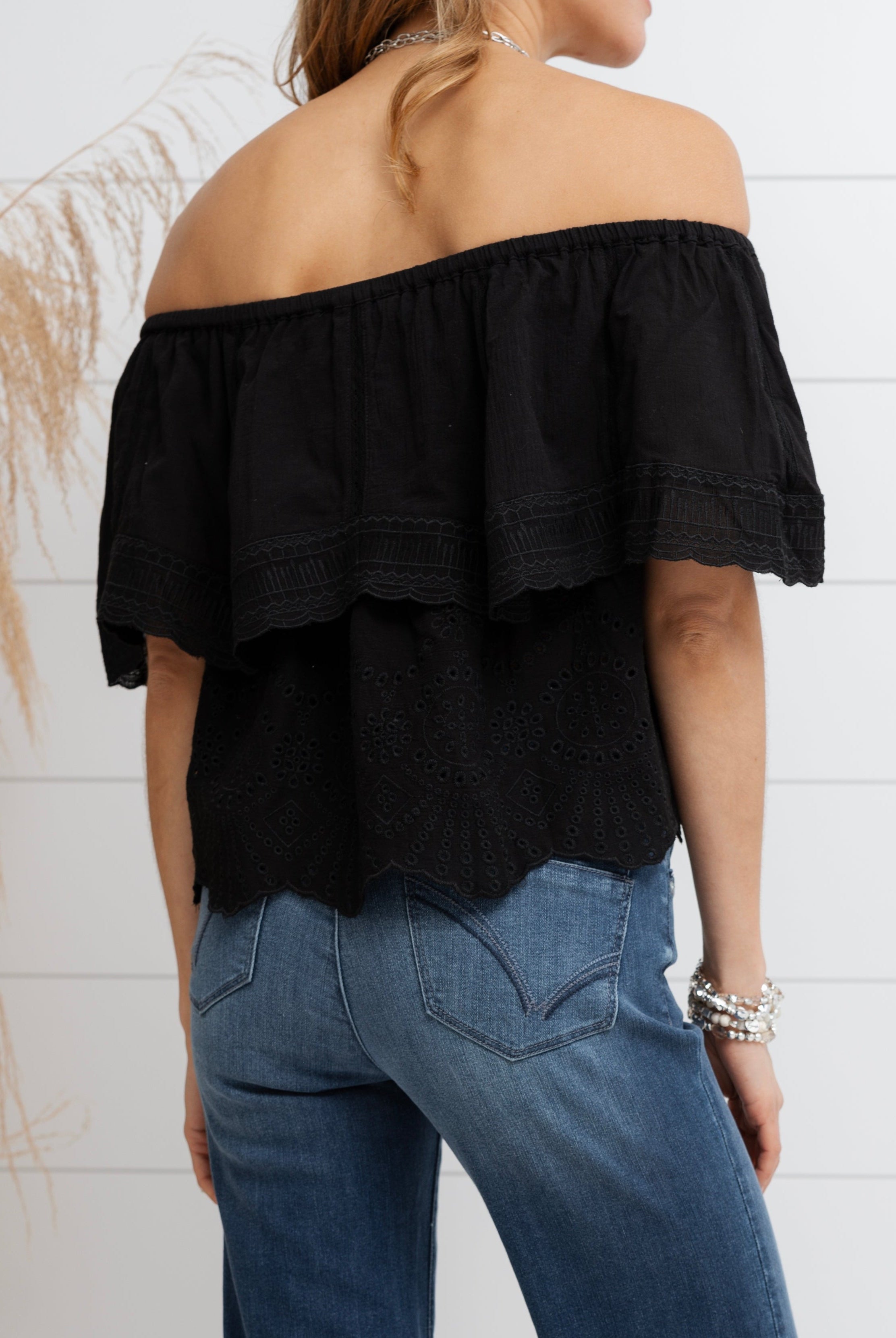 Person wearing a black off-shoulder top and blue jeans against a white background
