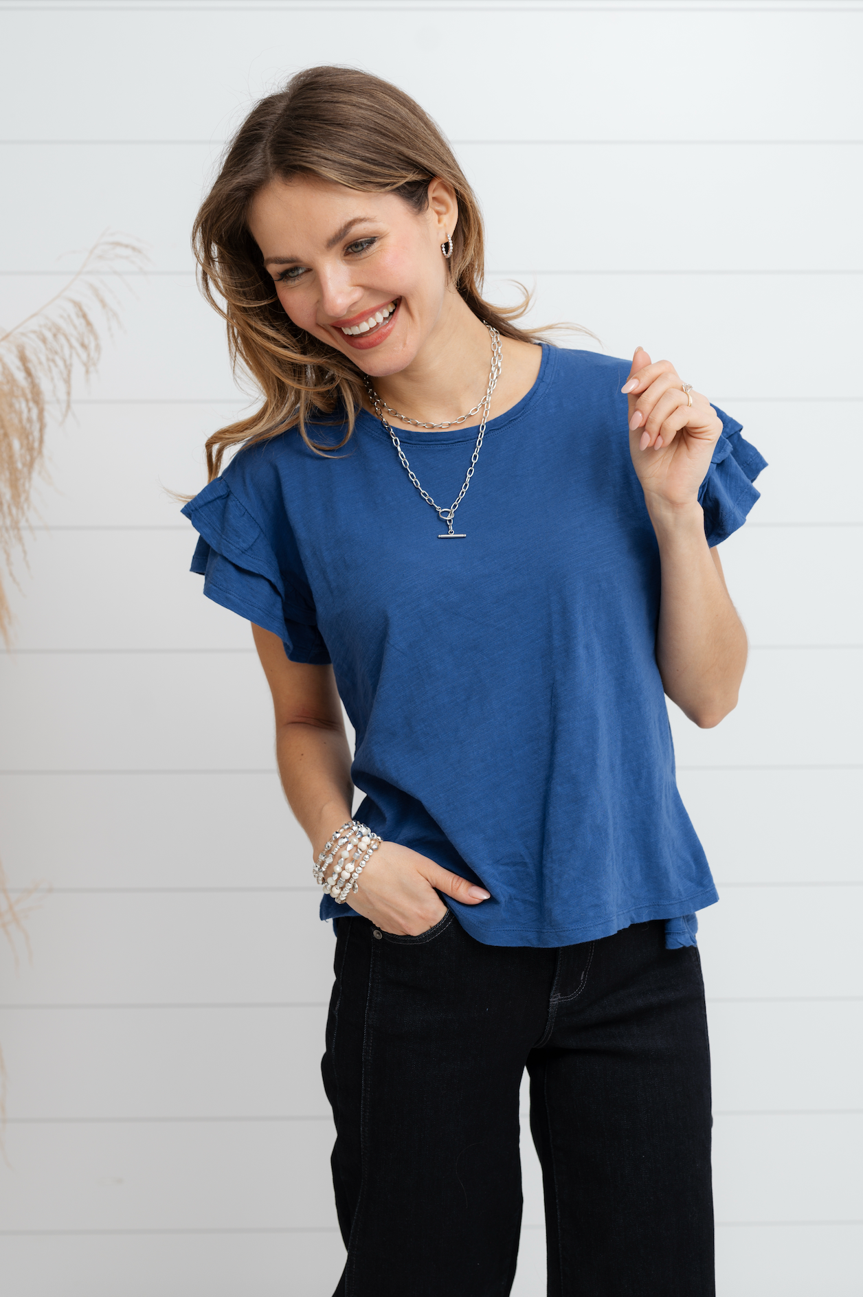 Woman wearing blue top and black jeans against a white background