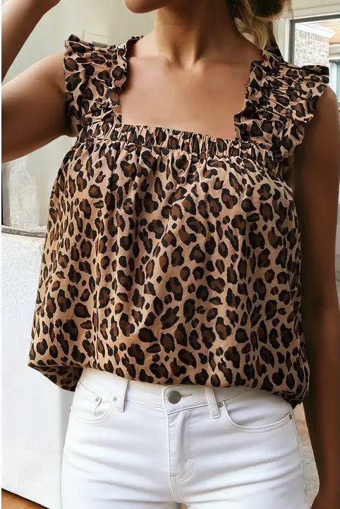 A woman wearing a leopard print ruffled top and white jeans, cropped from the chin down in an indoor setting.