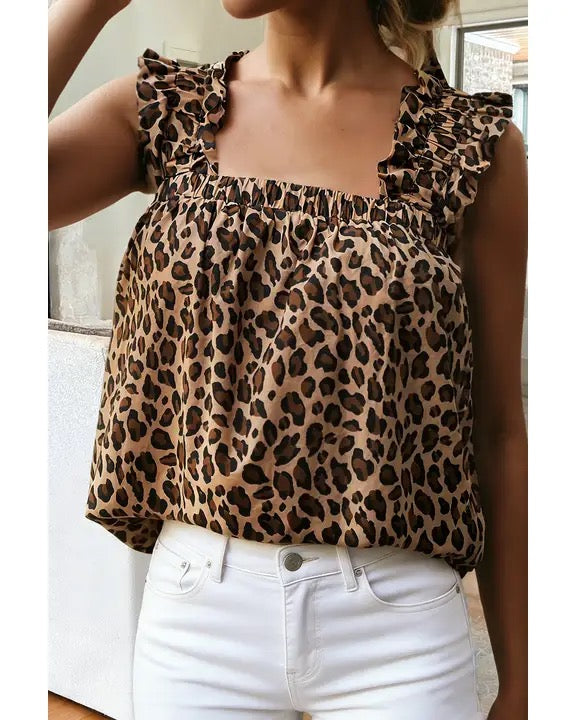 A woman wearing a leopard print ruffled top and white jeans, cropped from the chin down in an indoor setting.