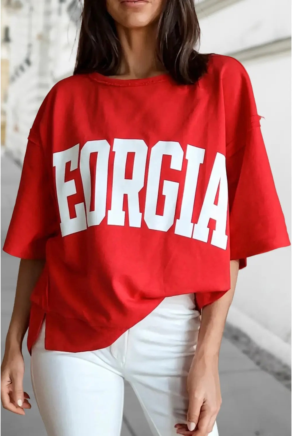 A woman wearing an oversized red t-shirt with 'GEORGIA' printed in bold white block letters across the front, paired with white pants.