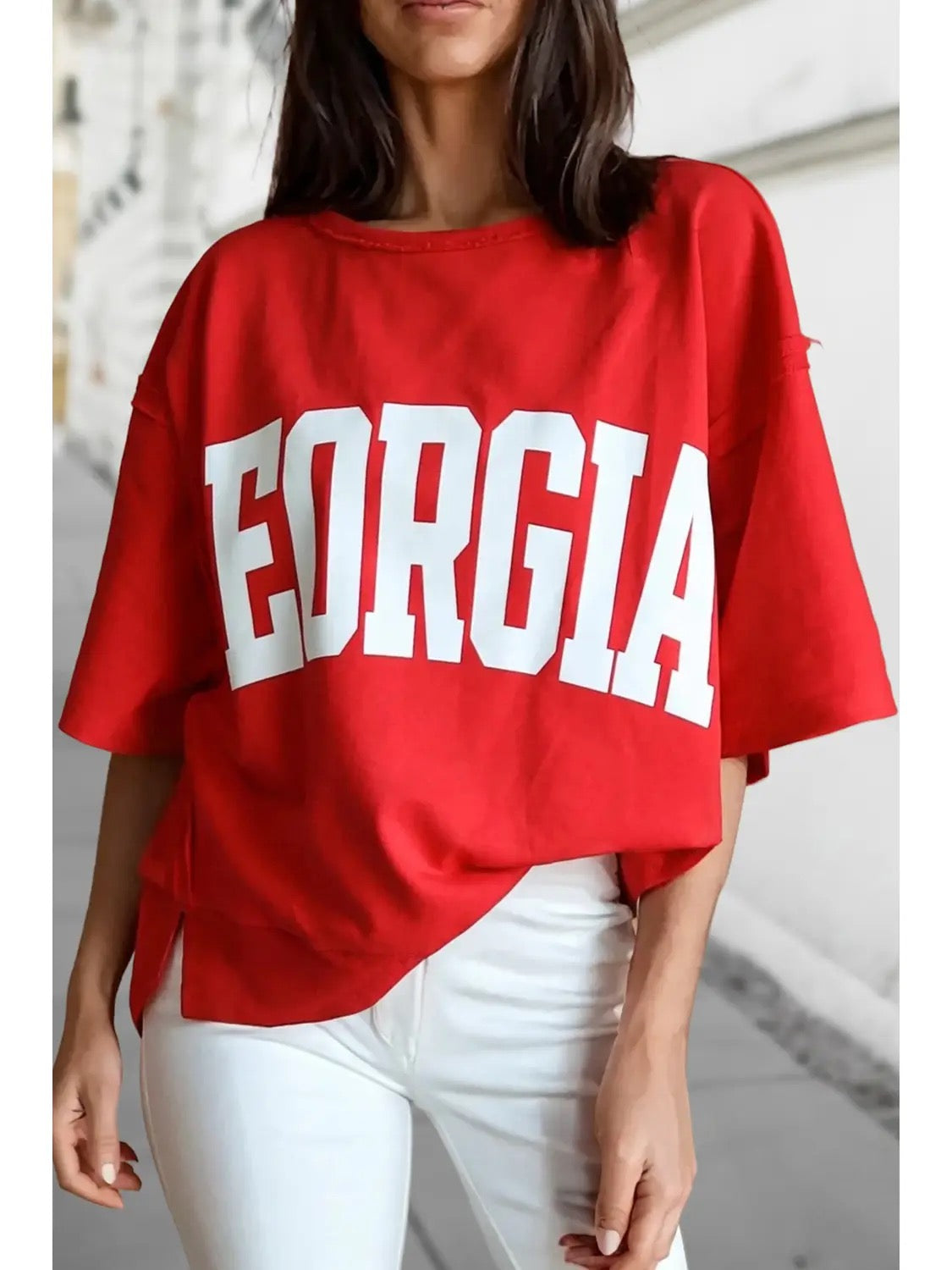 A woman wearing an oversized red t-shirt with 'GEORGIA' printed in bold white block letters across the front, paired with white pants.