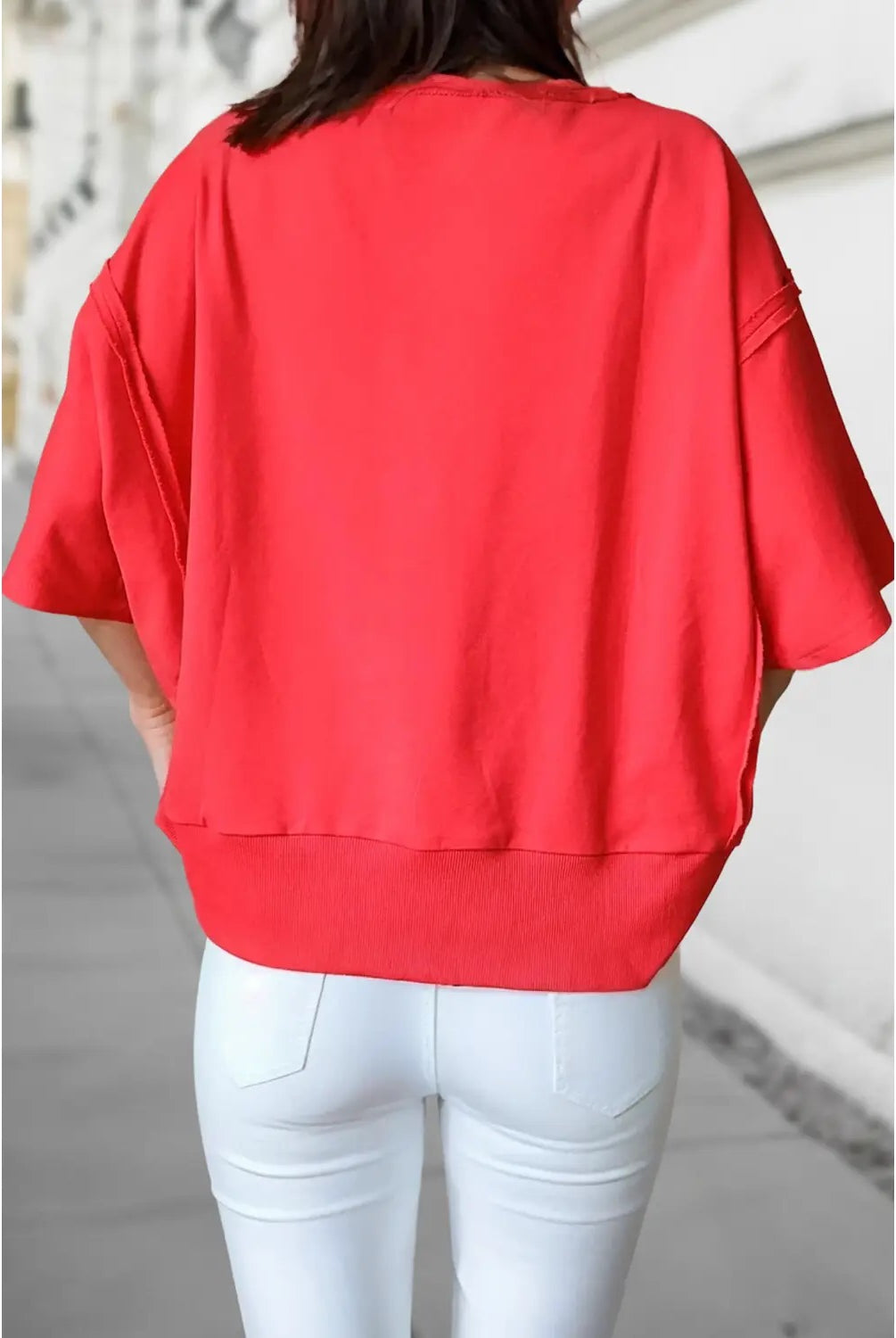 A person shown from the back wearing a loose-fitting bright red short-sleeve top and white pants in an outdoor setting.