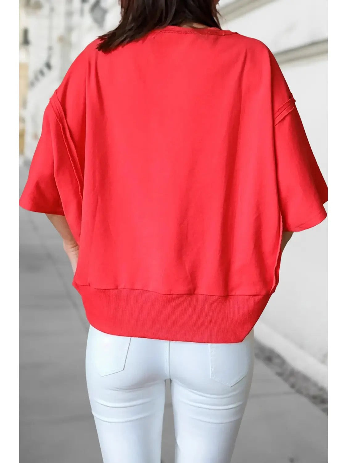 A person shown from the back wearing a loose-fitting bright red short-sleeve top and white pants in an outdoor setting.