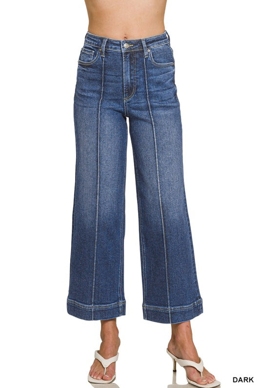 A model wearing a pair of dark blue wide-leg cropped jeans with front seam detailing, shown from the waist down on a white background.