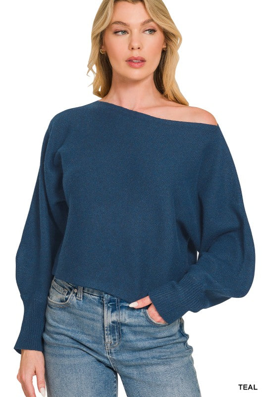 Woman wearing a teal off-shoulder sweater and blue jeans on a white background