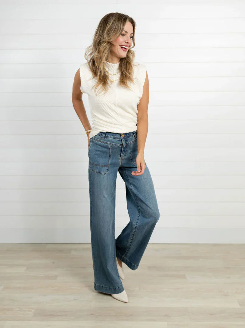 Model wearing jeans and a white tank against a white wall