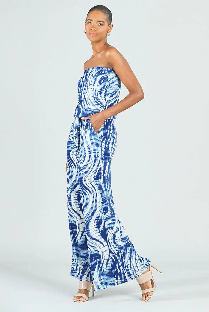A woman modeling a strapless blue and white patterned maxi dress with a tie-dye style design, standing against a light gray studio background.