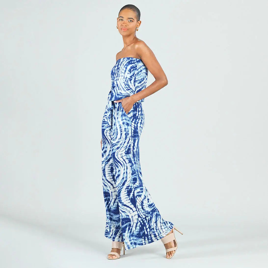 A woman modeling a strapless blue and white patterned maxi dress with a tie-dye style design, standing against a light gray studio background.