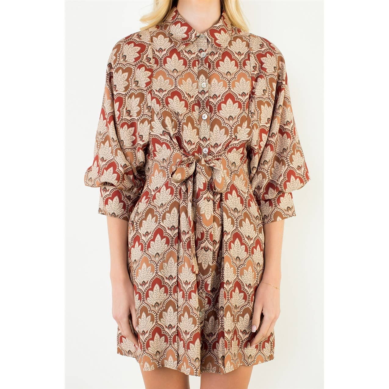 A woman wearing a short collared shirt dress with a beige, rust red, and brown geometric pattern, featuring three-quarter sleeves and a matching waist tie.