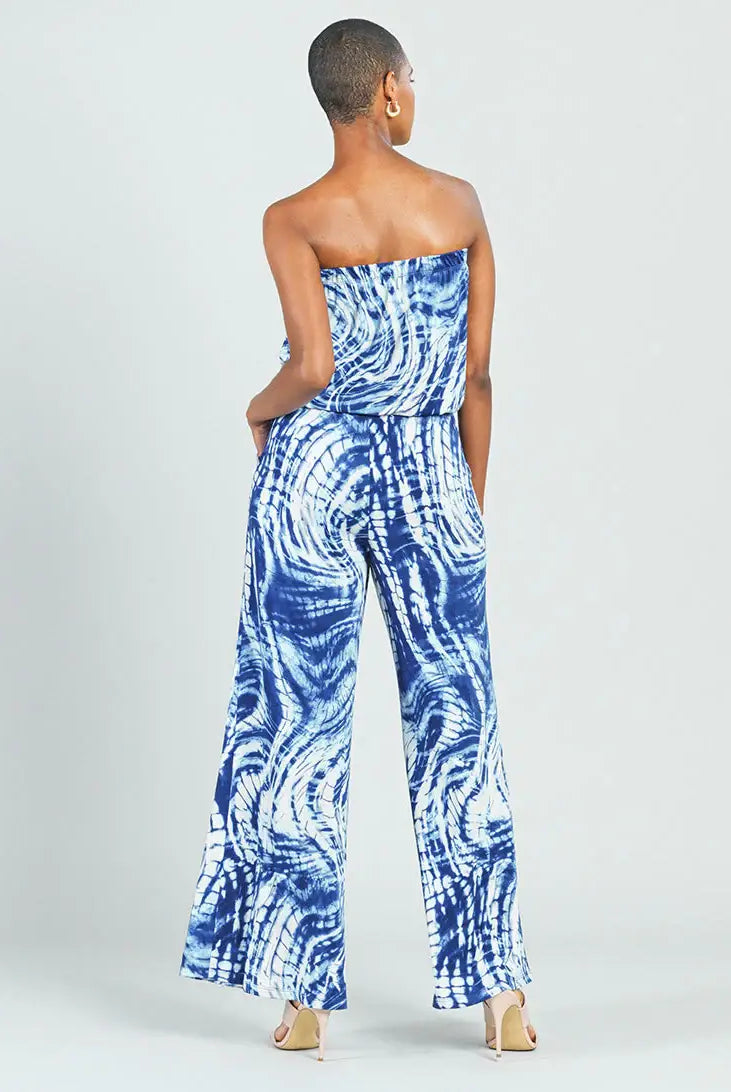 A woman shown from the back wearing a strapless wide-leg jumpsuit with a blue and white tie-dye swirl pattern, paired with beige high heels, against a light gray studio background.