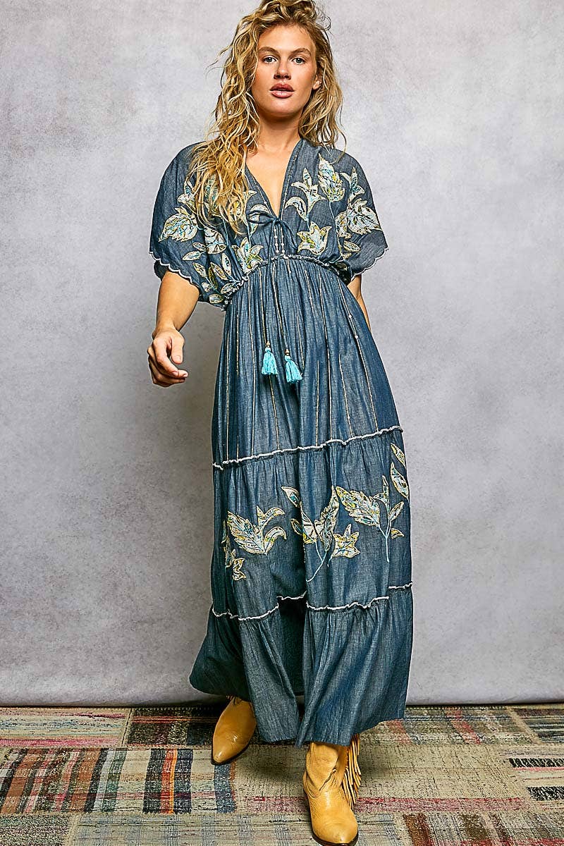 Woman wearing a blue floral dress with tassels against a gray background