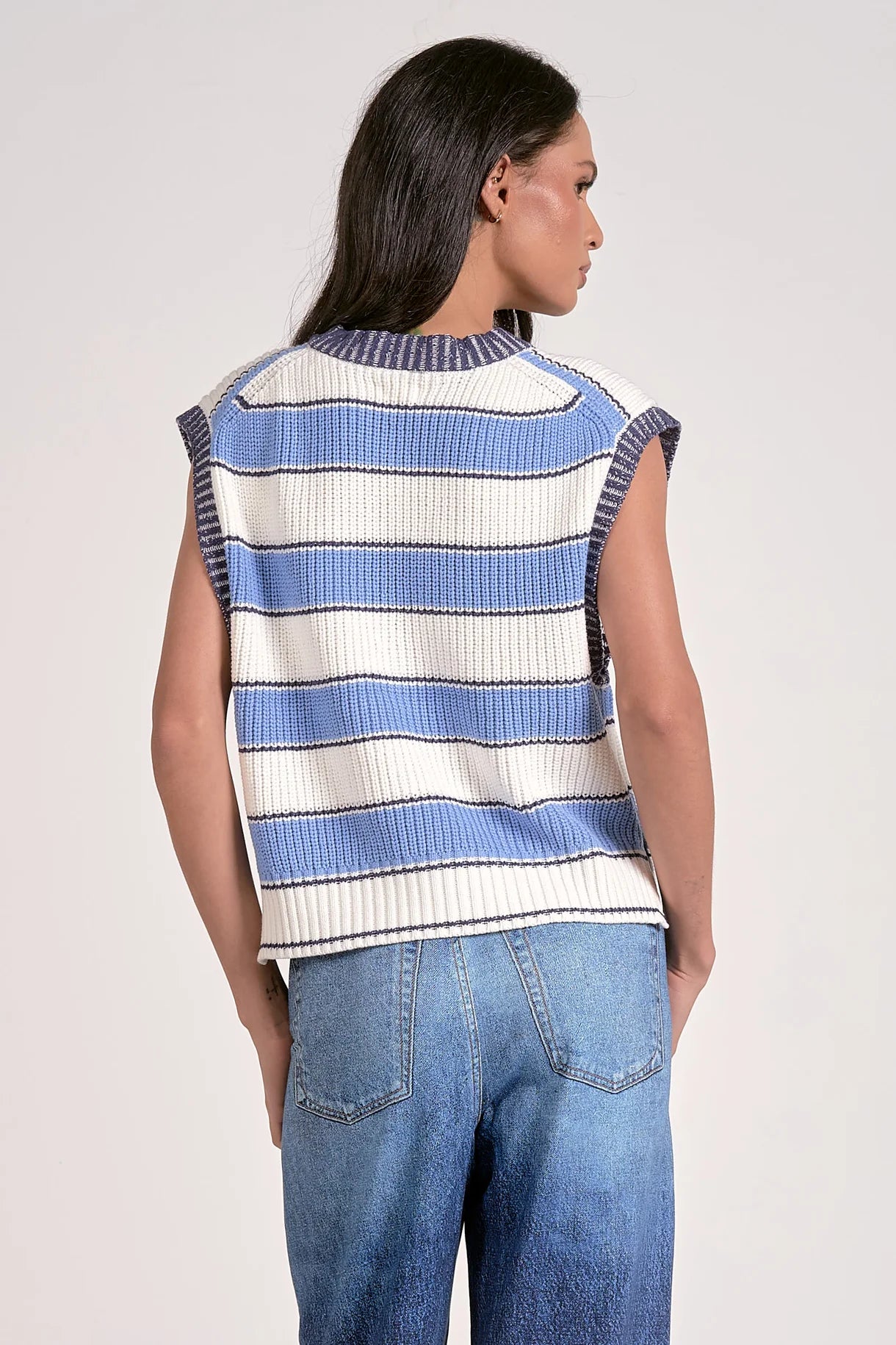 Woman wearing a sleeveless striped sweater and jeans on a plain background