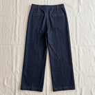 A pair of dark blue denim cropped pants shown from the back, laid flat on a wrinkled off-white fabric background.
