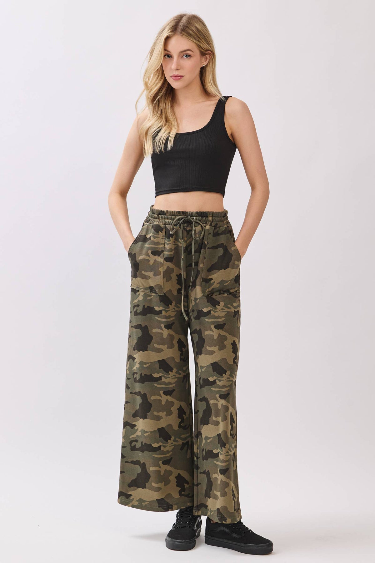 Woman wearing camouflage pants and a black top on a white background