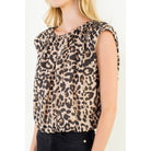 A woman wearing a sleeveless leopard-print top with a gathered, ruffled neckline and black pants, shown against a plain light background.