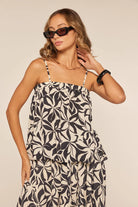 Woman wearing a black and white patterned top with sunglasses on a beige background