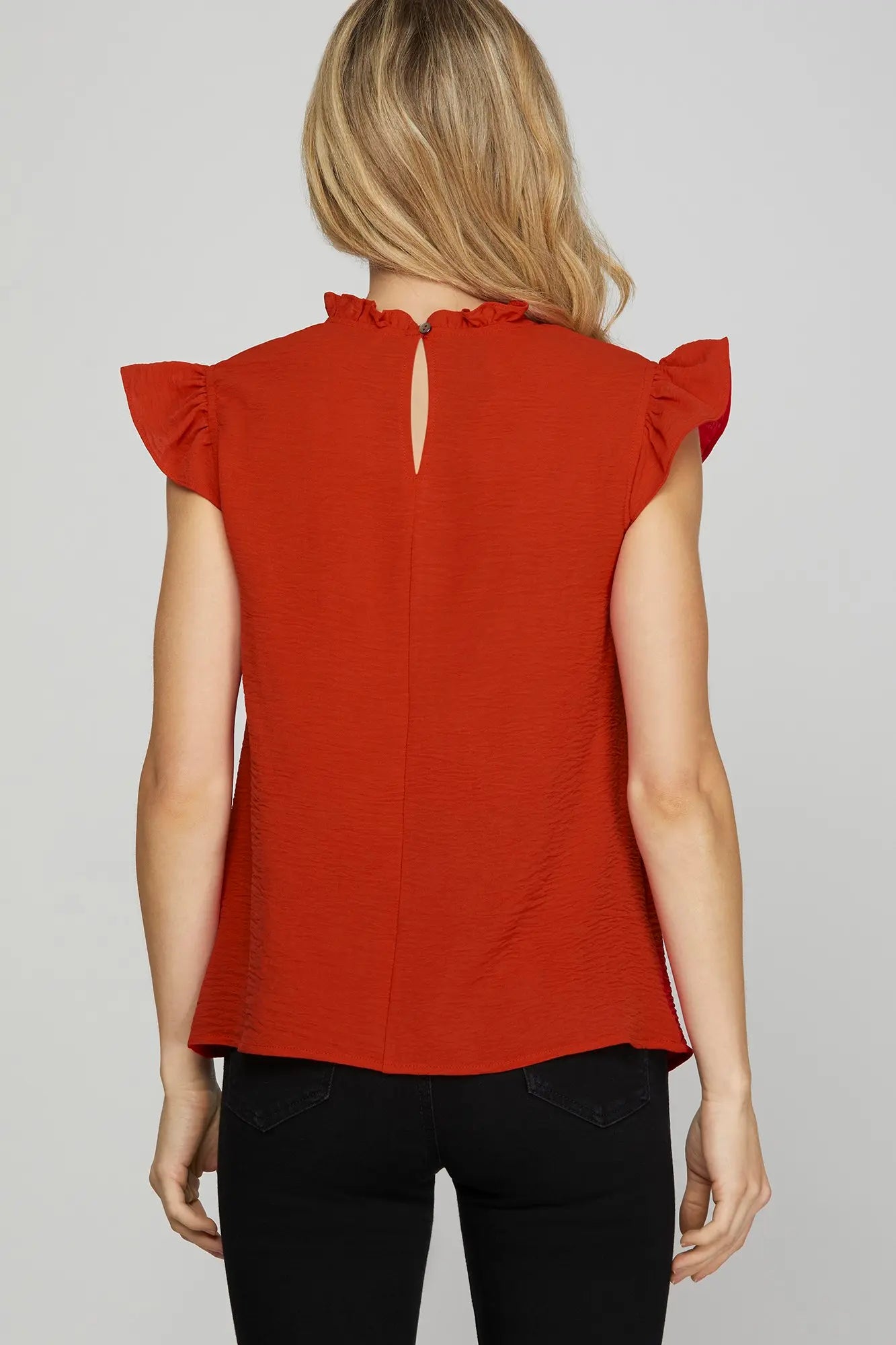 Back of woman wearing a red sleeveless top with ruffled shoulders 