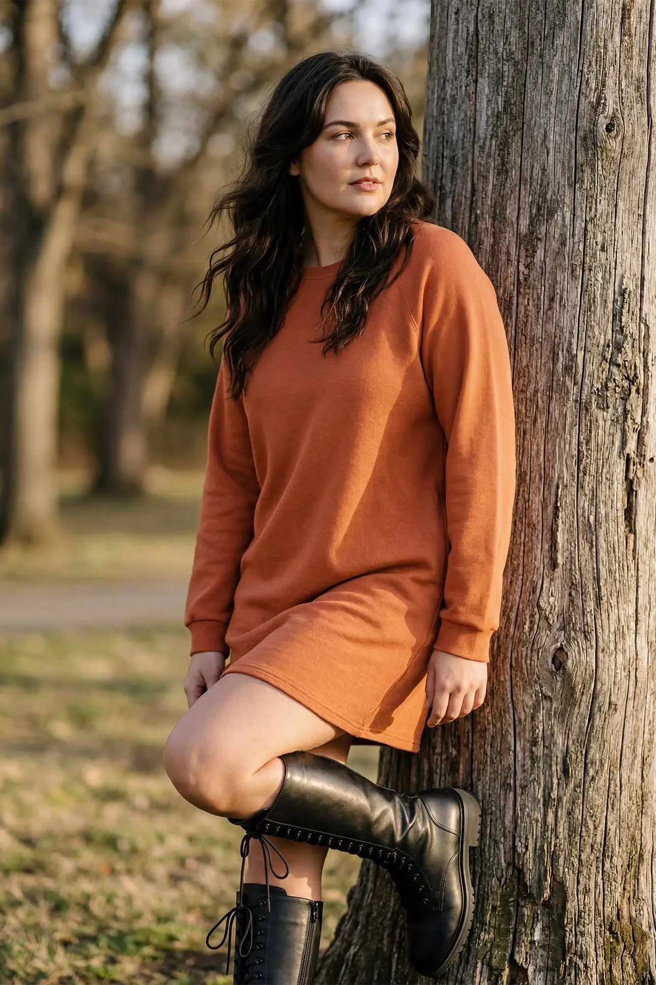 Model wearing orange dress and high boots against a tree