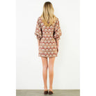 A woman viewed from behind wearing a short puff-sleeve dress with a beige, brown, and rust-red geometric pattern, standing against a plain white wall.