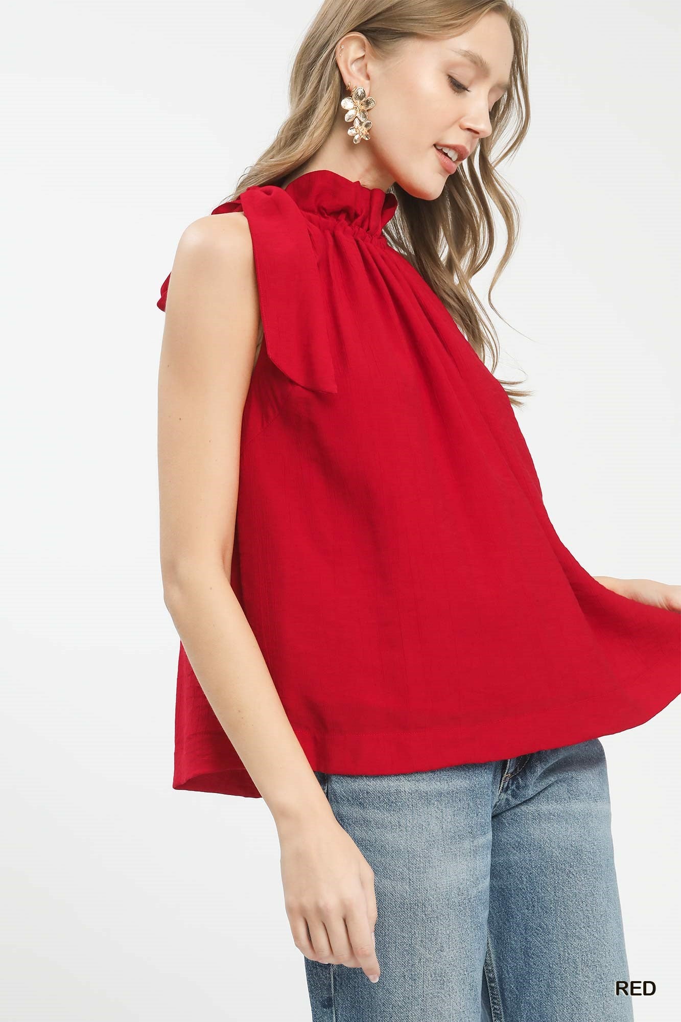 Woman wearing a red sleeveless top with a bow detail 