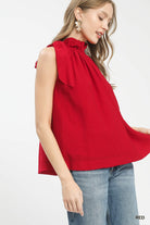 Woman wearing a red sleeveless top with a bow detail 