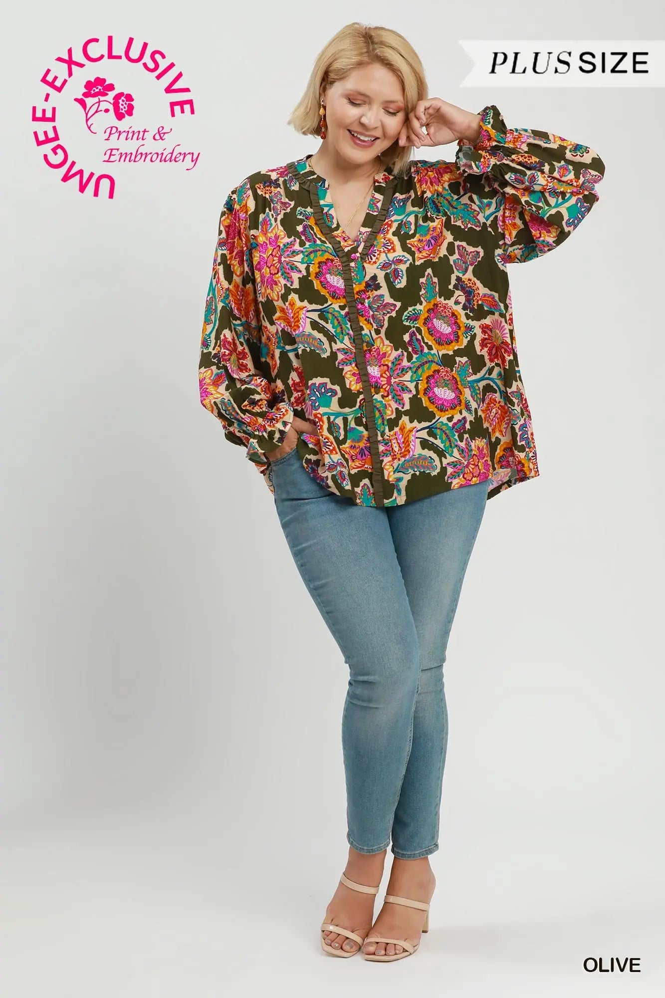 A woman modeling a long-sleeve button-up blouse with a dense floral and paisley print in olive green, pink, red, and blue, paired with blue jeans and beige heels on a light gray studio background. Text overlays include 'PLUS SIZE', 'OLIVE', and a pink 'UNBEZPREMIUM Print & Embroidery' logo.