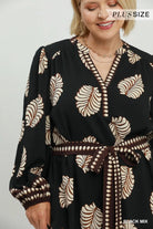 A woman wearing a black long-sleeve wrap dress with a beige and brown leaf pattern, a matching brown belt, and a V-neckline. The brand name 'PLUSSIZE' is visible in the top right corner.